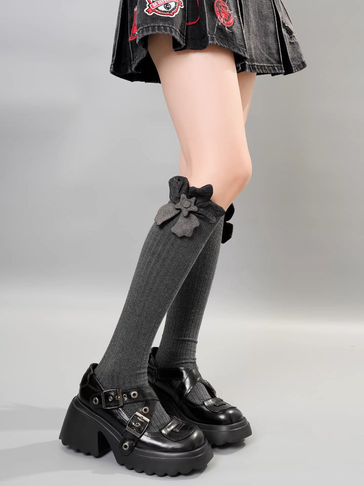 A person wearing gray knee-high socks with a gray flower embellishment and bow detail, paired with platform shoes.
