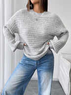 Full body shot of a woman in a light grey oversized knit sweater and blue denim jeans, hands on hips.