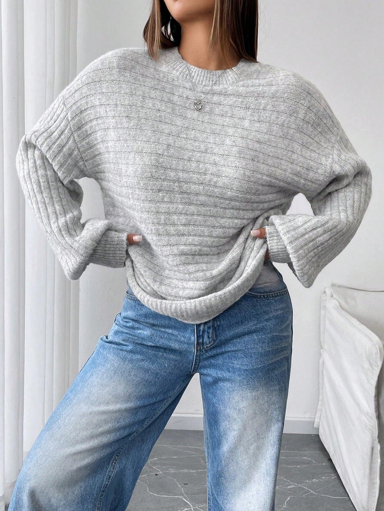 Full body shot of a woman in a light grey oversized knit sweater and blue denim jeans, hands on hips.