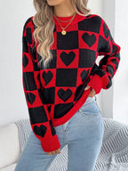 Close-up of a woman wearing a red and black checkerboard knit sweater with black heart patterns and light wash denim jeans.
