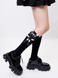 Person wearing black knee-high socks with a black and white cartoon cat applique, paired with black patent leather platform shoes.