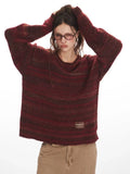 Woman posing with her hands on her head, wearing a maroon and brown striped oversized knit sweater with a small label on the side.