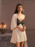Woman wearing a cream satin slip dress with black lace trim and a cream satin robe, standing in a room with candles.