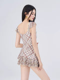 Rear view of a woman wearing a plaid print dress with cap sleeves and ruffled hem.