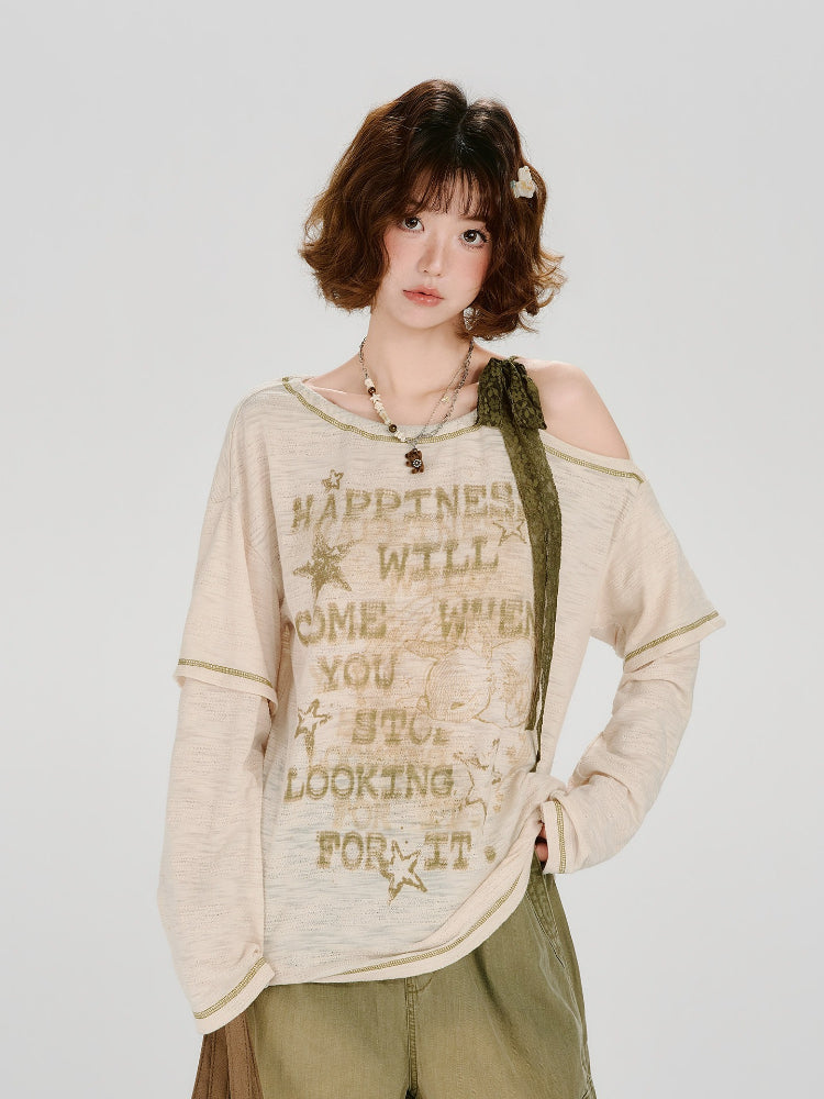Woman wearing a cream-colored long-sleeved graphic t-shirt with distressing and an off-the-shoulder detail.