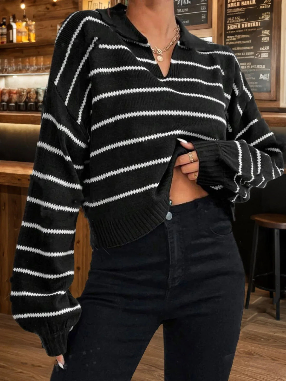 Woman wearing a black and white striped cropped knit sweater with a collared neckline and long sleeves.