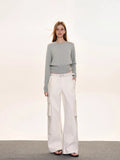 Woman wearing a light grey crew neck long sleeve cinched waist sweater and white wide leg pants