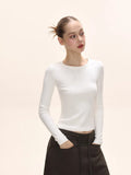 Woman posing with hands in pockets, wearing a white fitted long-sleeve shirt.