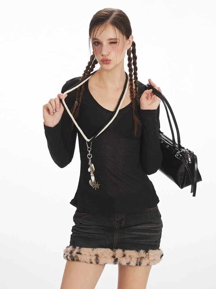 Close-up of a model wearing a black long-sleeve V-neck top and a distressed denim mini skirt with faux fur trim