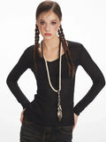 Model wearing a black long-sleeve V-neck top and distressed denim jeans, with a necklace