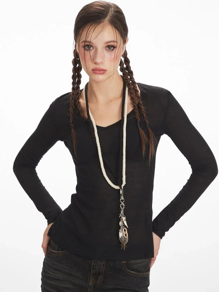 Model wearing a black long-sleeve V-neck top and distressed denim jeans, with a necklace