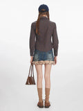 Back view of a woman in a plaid shirt and denim skirt with fur trim, holding a brown handbag.