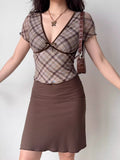 Full body shot of a woman wearing a brown plaid fitted top with short sleeves and a matching brown skirt.