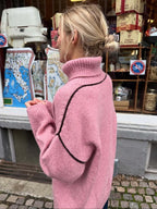 Back view of a woman in a pink turtleneck sweater with dark seam accents