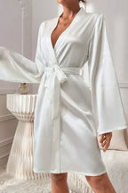 Woman wearing a white satin robe with bell sleeves and a self-tie belt.