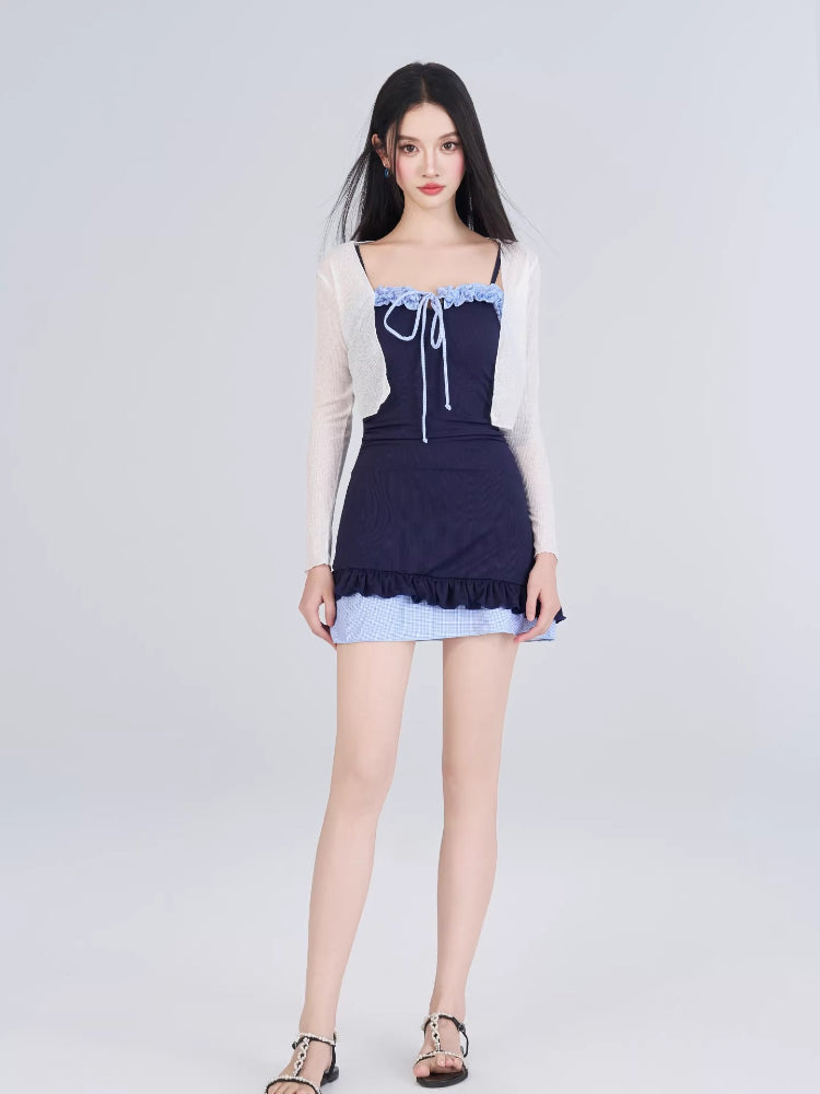 Woman in navy one-piece swimsuit with blue gingham skirt overlay and white sheer cardigan