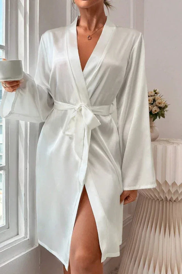 Woman holding a cup and wearing a white satin robe with bell sleeves and a self-tie belt.