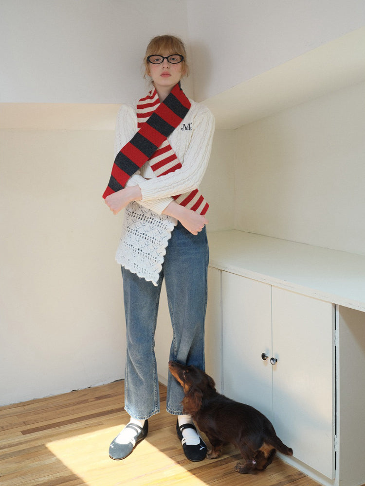 Model wearing a white sweater with an embroidered initial, blue jeans, and a red, gray, and white striped scarf.