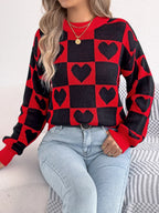 Woman wearing a red and black checkerboard knit sweater with black heart patterns and light wash denim jeans.