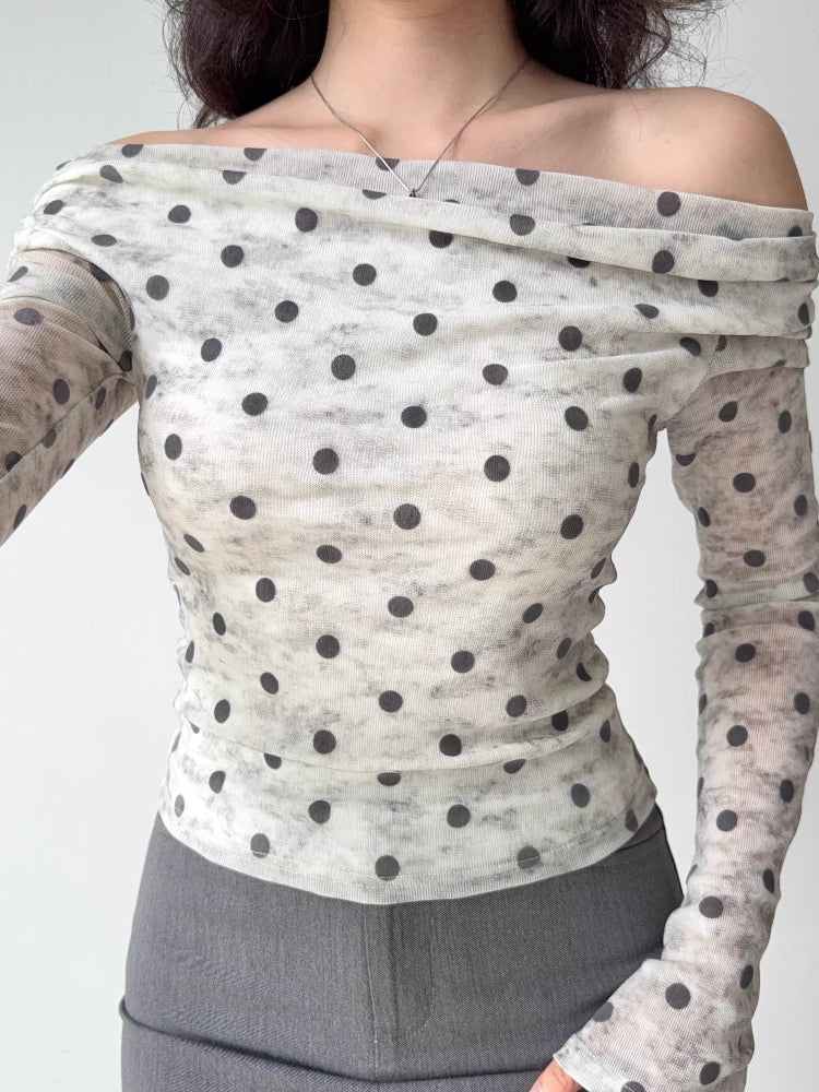 Woman wearing a white and grey polka dot sheer mesh off-the-shoulder top with long sleeves.