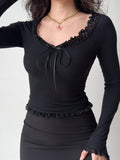 woman wearing a black off-the-shoulder ribbed knit top with lace trim and a tie closure at the neckline, paired with a black skirt