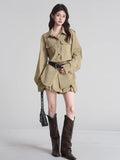 Woman wearing a khaki shirt dress, black studded belt, and brown boots against a neutral background.