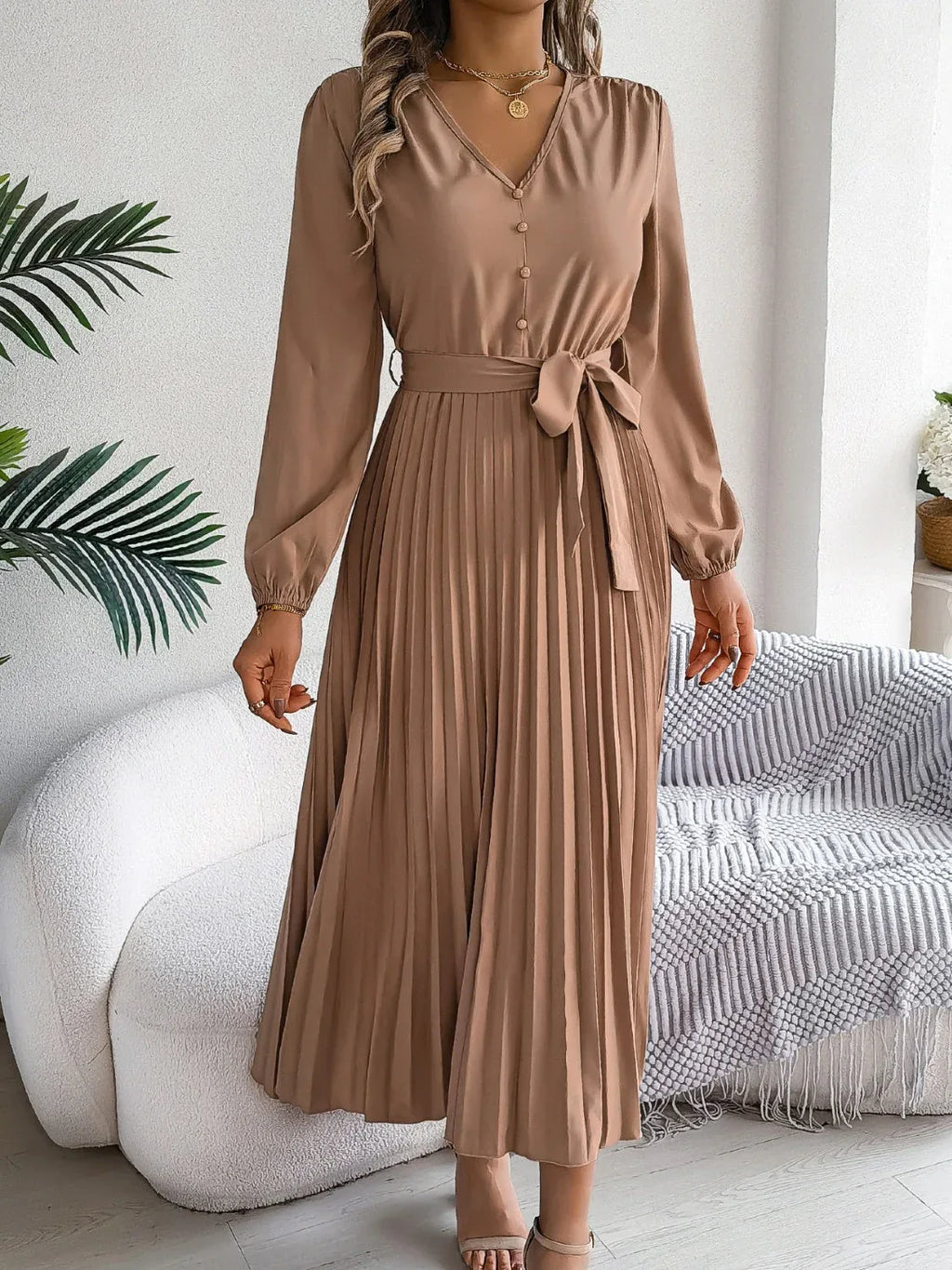 Woman in a brown long-sleeve V-neck midi dress with a pleated skirt and a self-tie belt, holding her hair