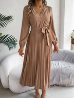 Woman in a brown long-sleeve V-neck midi dress with a pleated skirt and a self-tie belt, holding her hair