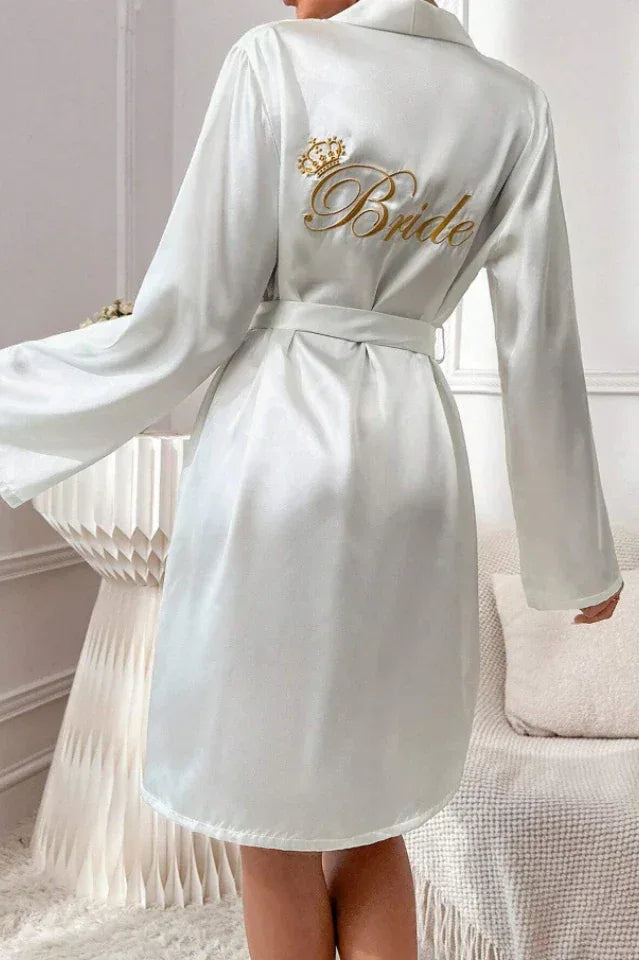 Back view of a woman wearing a white satin robe with 'Bride' embroidered on the back.