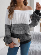 Woman holding a handbag while wearing an off-the-shoulder color block knit sweater.