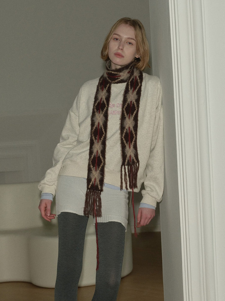 Model posing with a cream sweatshirt and a fringed argyle scarf.