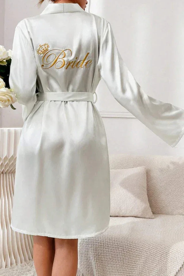 Woman holding flowers and wearing a white satin robe with 'Bride' embroidered on the back.