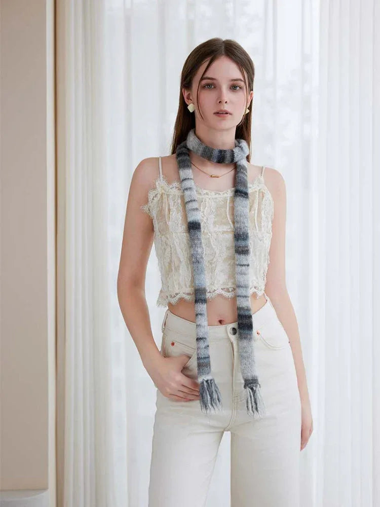 Woman wearing a white lace camisole and cream pants, accessorized with a long, striped knit scarf in shades of grey and black.