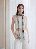 Woman wearing a white lace camisole and cream pants, accessorized with a long, striped knit scarf in shades of grey and black.