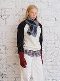 Close-up of a model wearing a cream and black raglan sleeve sweater, plaid shirt, white pants, and a blue argyle scarf.