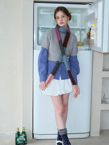 Woman wearing a grey cropped sweater over a blue gingham shirt, white bubble hem skirt, and a colorful striped scarf.