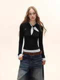 Model wearing a black long-sleeve top with white polka dot trim and scarf detail