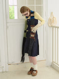 Woman adjusting a multi-colored striped fuzzy scarf with fringe details, worn with a yellow long-sleeve top, navy camisole, and denim skirt.