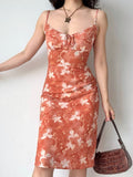 Side view of a woman holding a brown handbag while wearing an orange floral print midi dress.