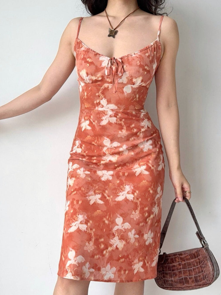 Side view of a woman holding a brown handbag while wearing an orange floral print midi dress.