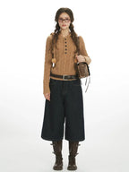Woman wearing a brown hooded cable knit sweater with a button-up placket and drawstring hood with pom-poms