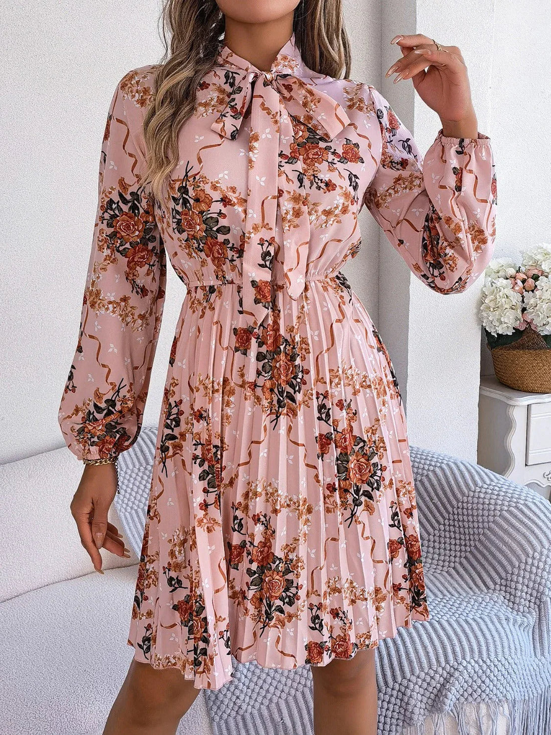 Woman wearing a pink floral print midi dress with a bow neckline and pleated skirt