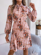 Woman wearing a pink floral print midi dress with a bow neckline and pleated skirt
