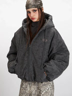 Woman in a charcoal grey textured puffer jacket with hands in pockets.