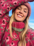 Woman with blonde hair wearing a pink floral knit turtleneck sweater and pink beanie