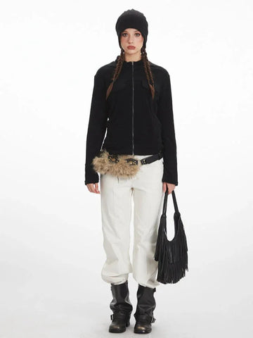 Woman wearing a black zip-up fleece jacket, white pants, black boots, and a black beanie.