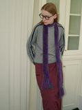Woman wearing a gray sweatshirt, maroon skirt, and a purple and green fuzzy scarf with fringed ends, looking to the side.