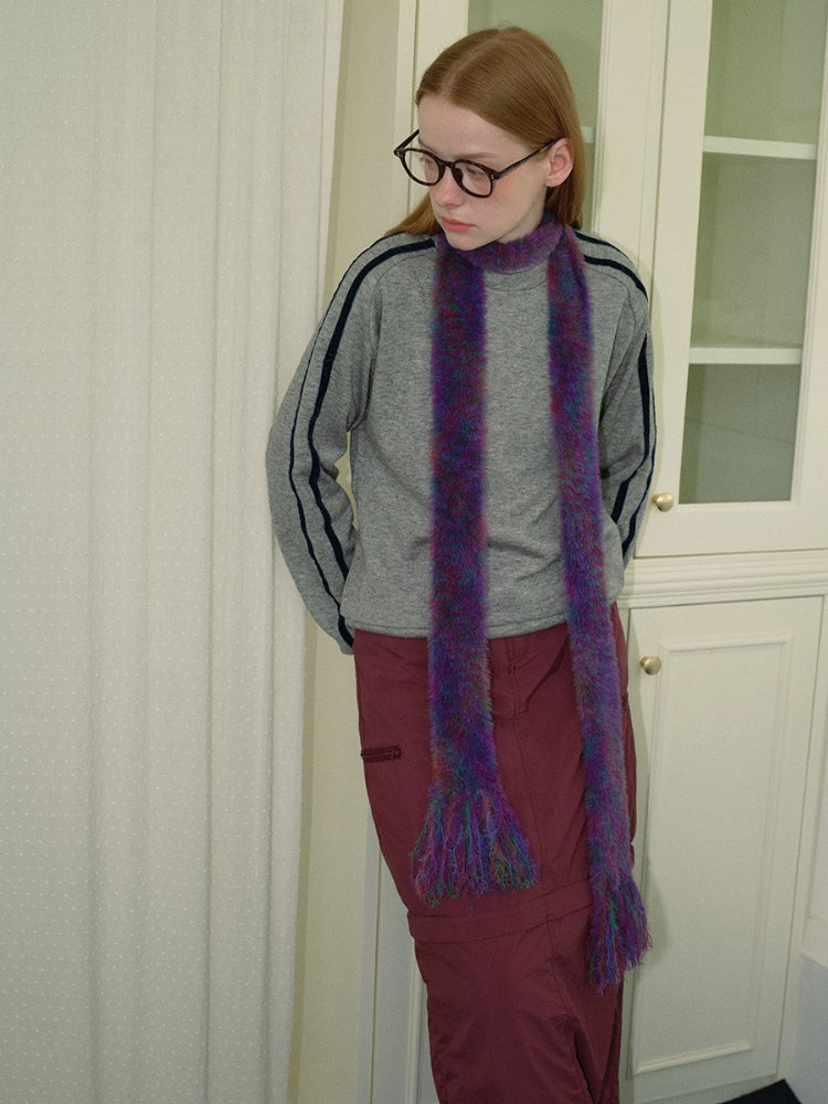 Woman wearing a gray sweatshirt, maroon skirt, and a purple and green fuzzy scarf with fringed ends, looking to the side.