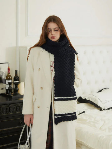 Woman wearing a navy and white striped knit scarf over a white coat.