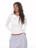 Full body shot of a woman wearing a white fitted long-sleeve top and casual grey pants.